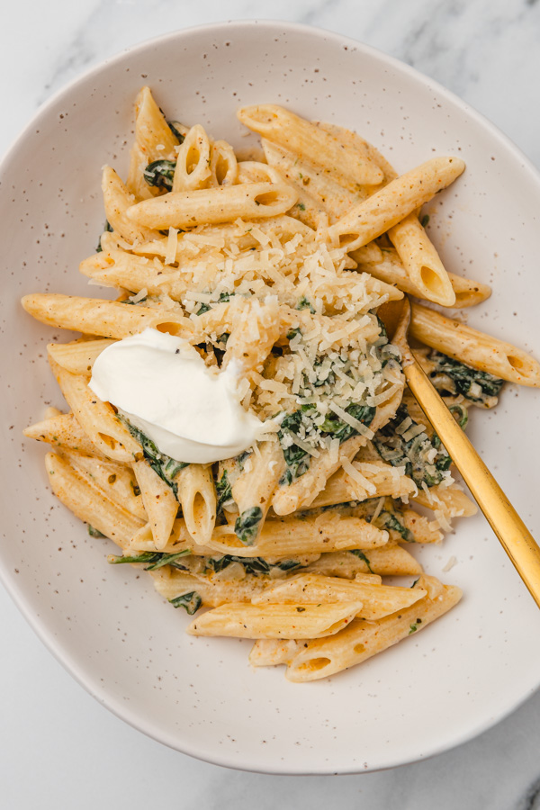a bowl of penne pasta garnished with a dollop of sour cream and grated parmesan cheese.