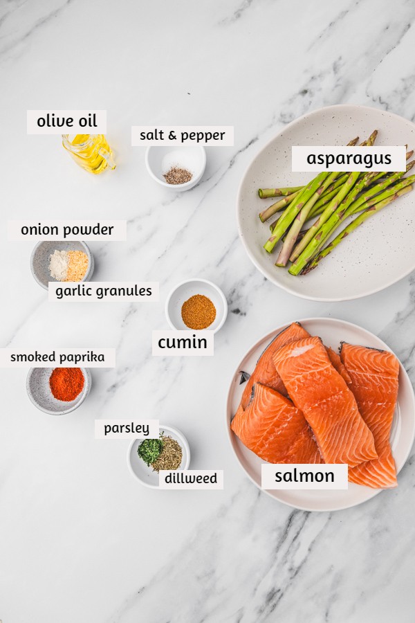 ingredients to cook salmon and asparagus on a white marble surface.