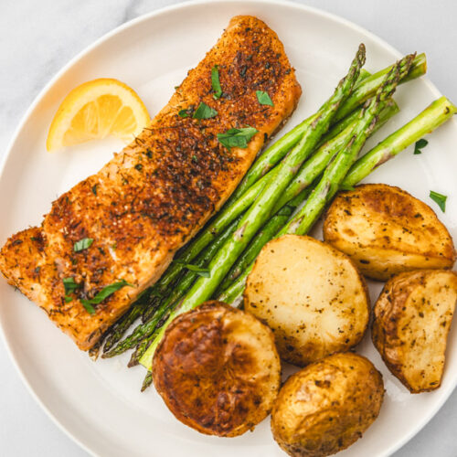 salmon fillet with asparagus, baked potatoes and a lemon wedge on a white plate.