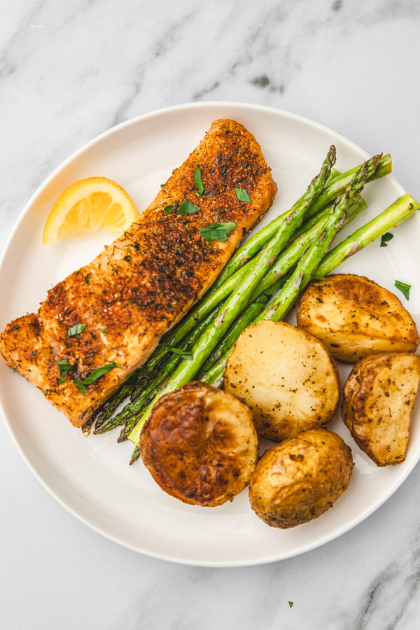 salmon fillet with asparagus, baked potatoes and a lemon wedge on a white plate.