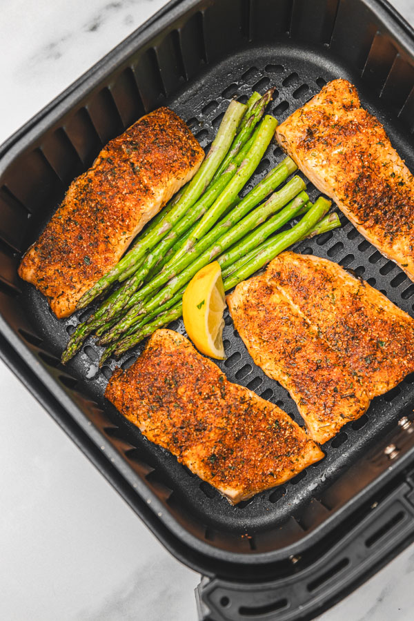 asparagus and salmon with lemon wedge in an air fryer basket.