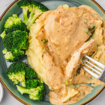 a plate of chicken with cream sauce and mashed potatoes with broccoli.