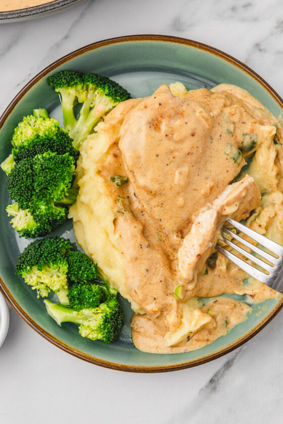 a plate of chicken with cream sauce and mashed potatoes with broccoli.