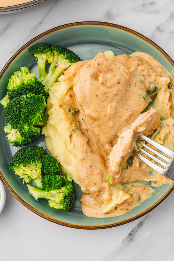 a plate of chicken covered in a creamy sauce with some broccoli on the side.