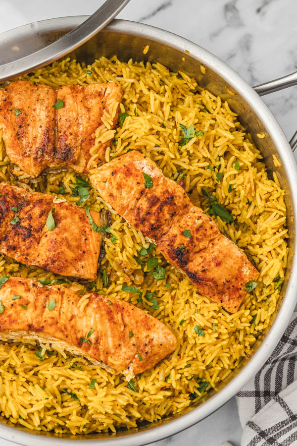 garlic turmeric rice and salmon in a skillet partially covered with a lid.