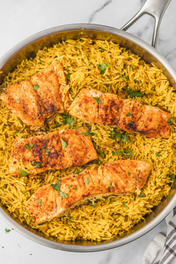 salmon and yellow rice in a skillet garnished with chopped parsley.