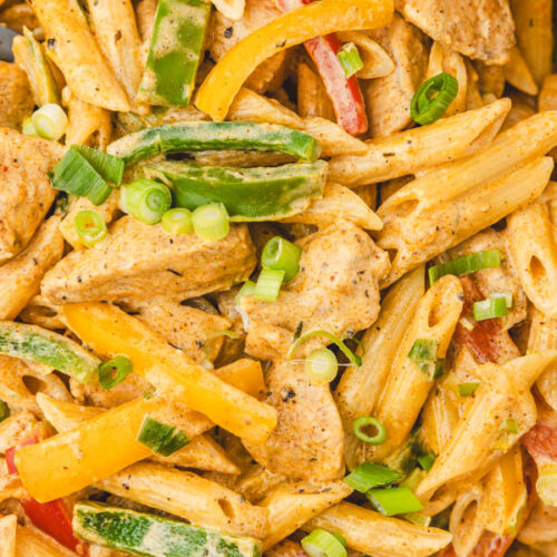 a close up on jerk chicken pasta garnished with sliced green onions.