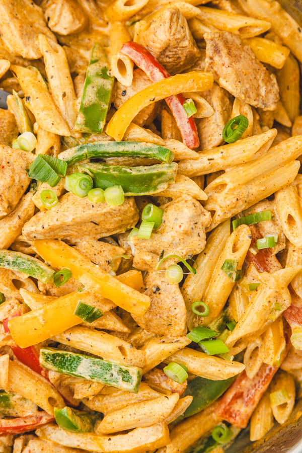 a close up on jerk chicken pasta garnished with sliced green onions.