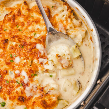 cauliflower cheese in a baking dish placed in an air fryer basket.