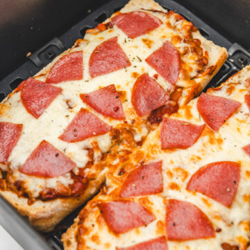 two slices of bread pepperoni pizza in an air fryer basket.