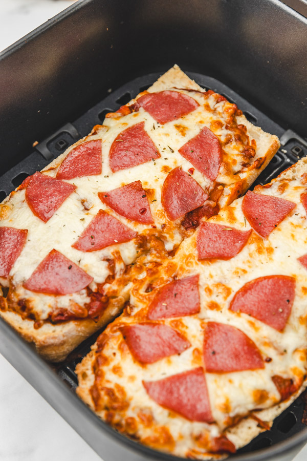 a close up of french bread pizza in an air fryer basket.