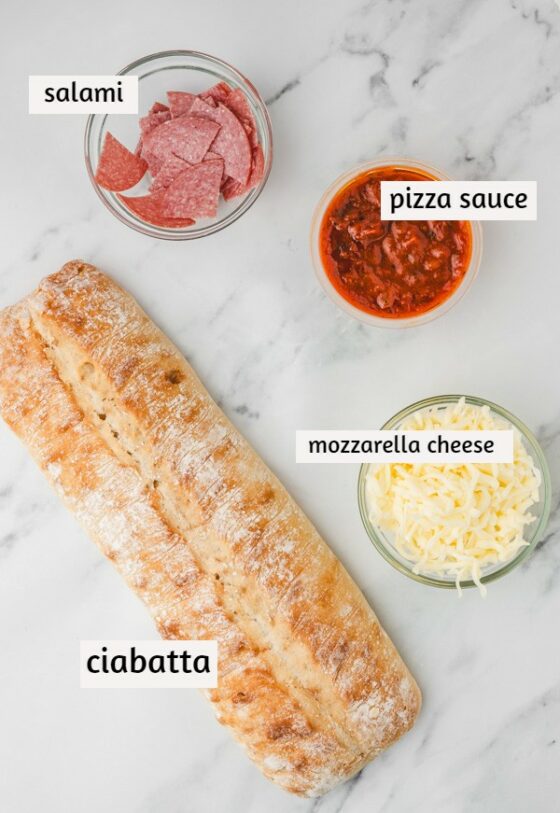 ingredients to make pizza bread laid on a white marble surface.