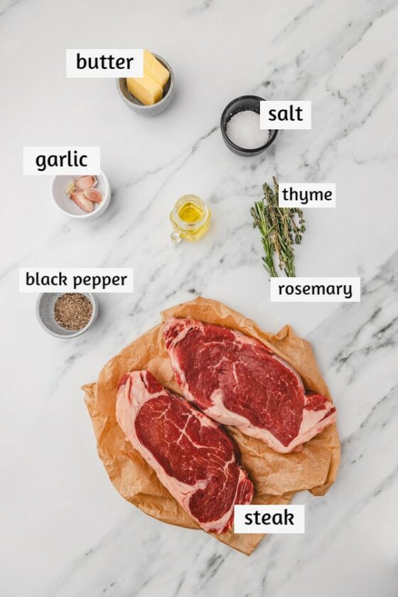 ingredients to cook steak laid on white marble surface.