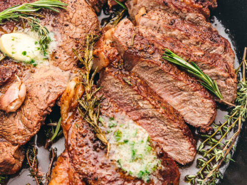 sliced sirloin steak topped with garlic butter and fresh herbs in a cast iron skillet/