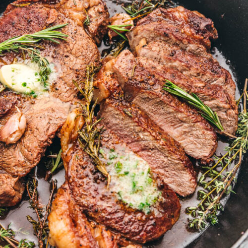 sliced sirloin steak topped with garlic butter and fresh herbs in a cast iron skillet/
