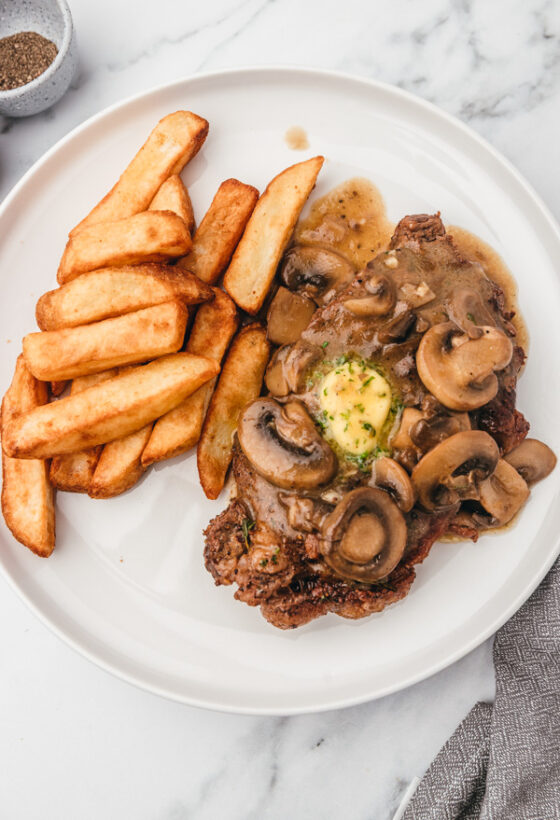 a plate of thick fries and steak topped with mushroom sauce.