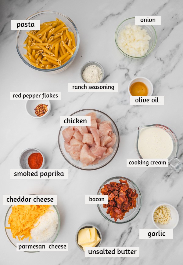 ingredients needed to make a creamy pasta with chicken on a white marble surface.