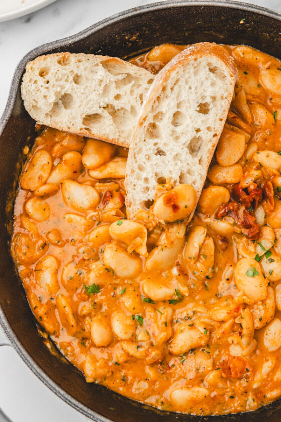 two slices of bread placed on butter beans in a skillet.