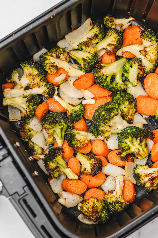 cooked broccoli, carrots and onions in an air fryer basket.