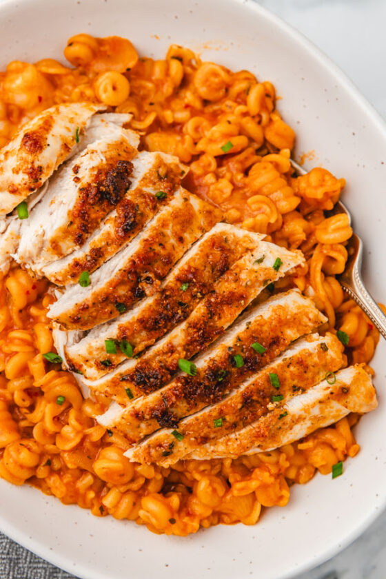 sliced chicken breasts sitting on a bed of pasta in a white bowl.
