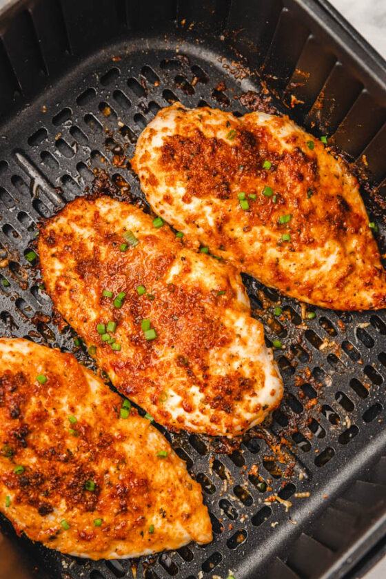 three cooked chicken breasts in air fryer basket garnished with chopped chives.