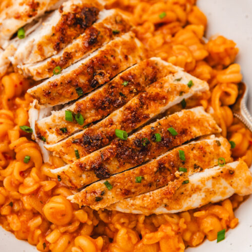 sliced chicken breast placed on a bed of pasta in a white bowl.
